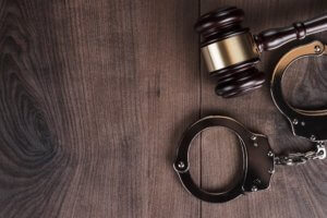 handcuffs and judge gavel on brown wooden background